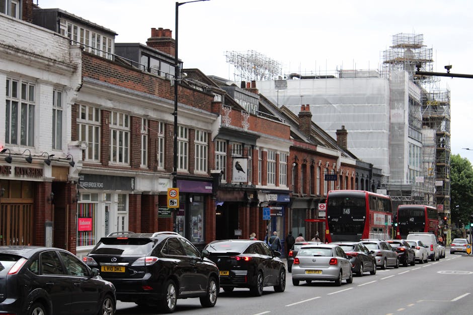 A row of Victorian terraced houses on Amersham Road, New Cross, with brick facades, large sash windows, and black wrought iron railings in front. The pavement runs parallel to the houses, with a narro