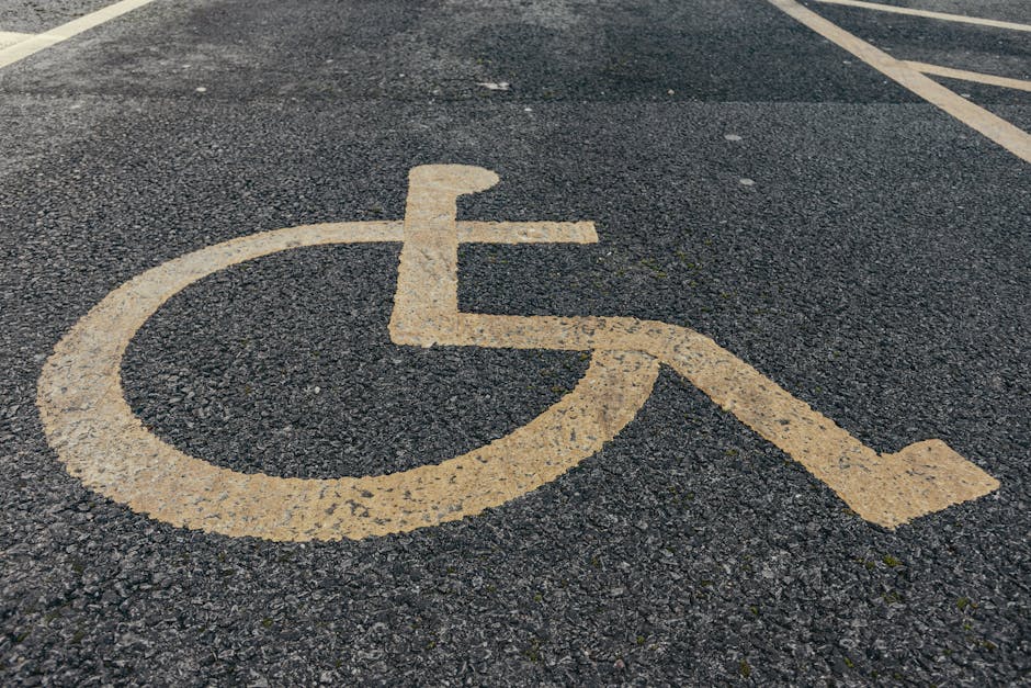 A black metal directional signpost with multiple rectangular signs attached, each pointing in different directions and labeled with white text for locations such as Biggleswade Common, Library, Railway Station, Police Station, Council Offices, Bus Waiting Facility, and Toilets. The signs feature pedestrian icons, with some signs including additional symbols like a wheelchair accessibility icon. The signpost stands outdoors against a backdrop of leafy green trees and an overcast sky, indicating a public area or neighbourhood environment observed during daylight. This setting may be relevant to home relocation or moving logistics, such as navigating to different local facilities during a house move, with Man and Van New Cross providing related removals and transport services.